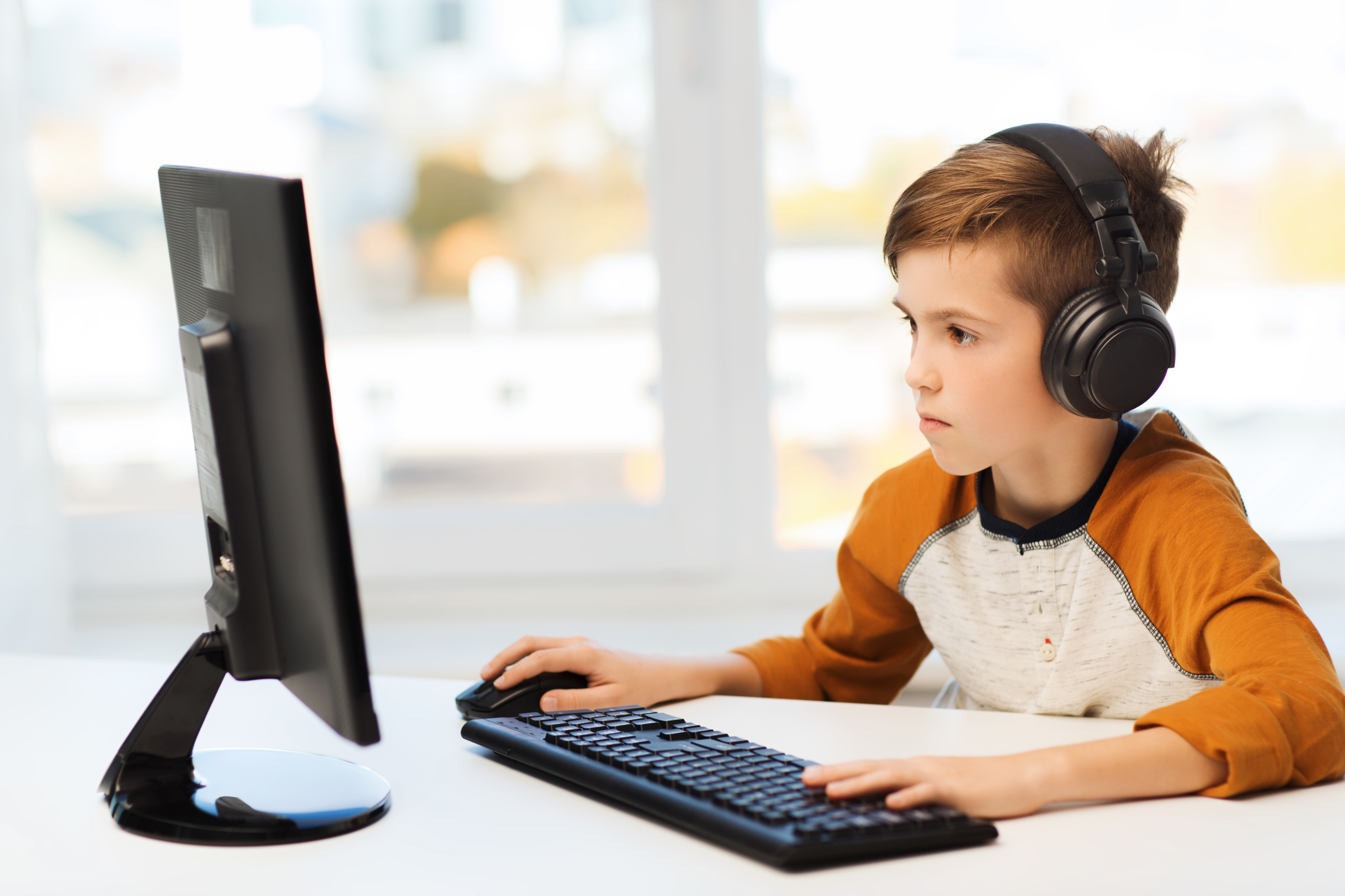 leisure, education, children, technology and people concept - boy with computer and headphones typing on keyboard or playing video game at home