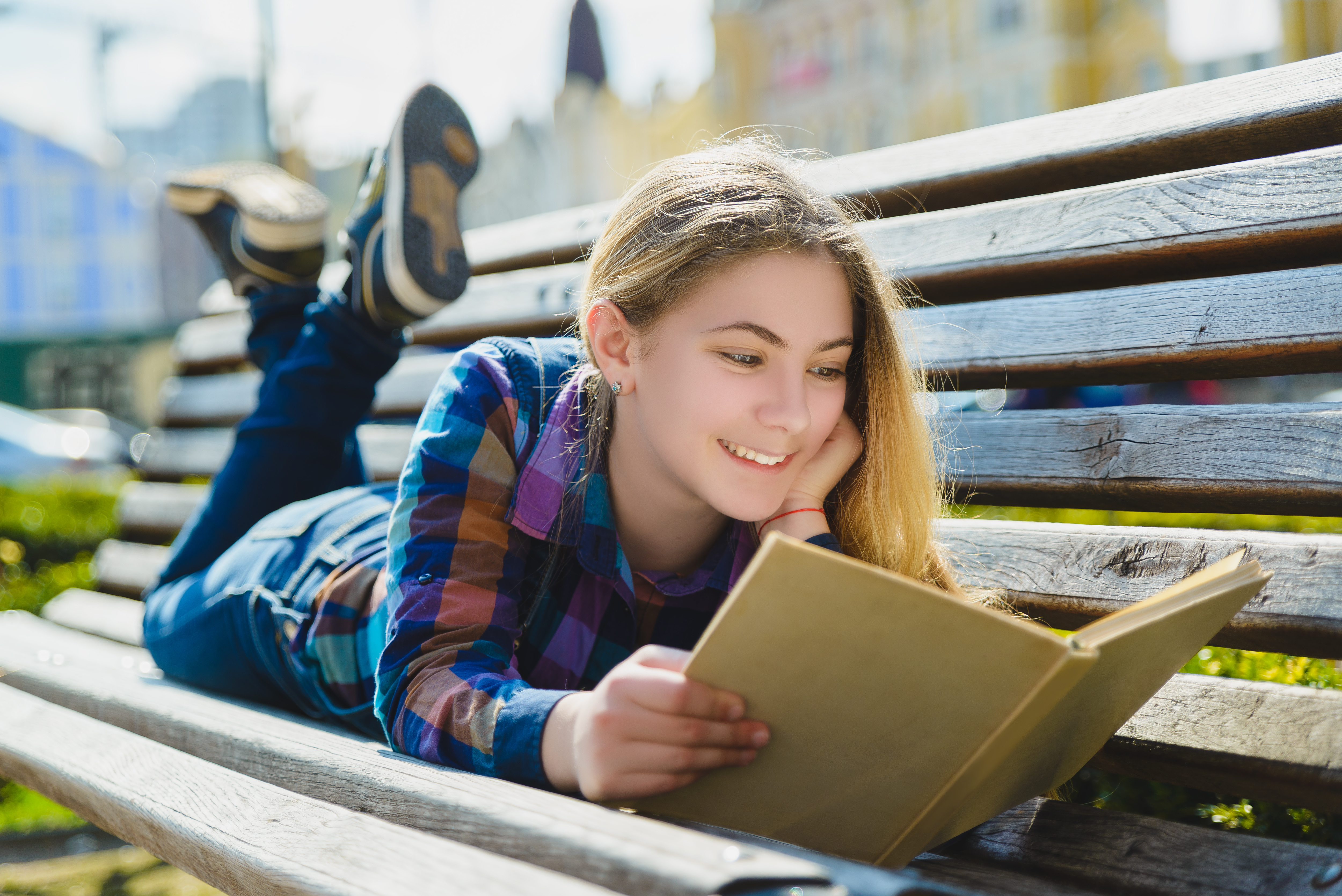 Little pretty girl reading a book and sitting on bench outdoor.